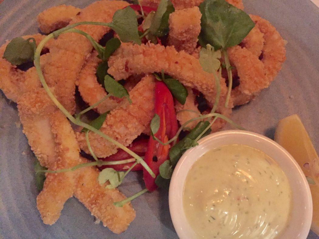 breaded calamari with red peppers, greens and a sauce on a blue plate 
