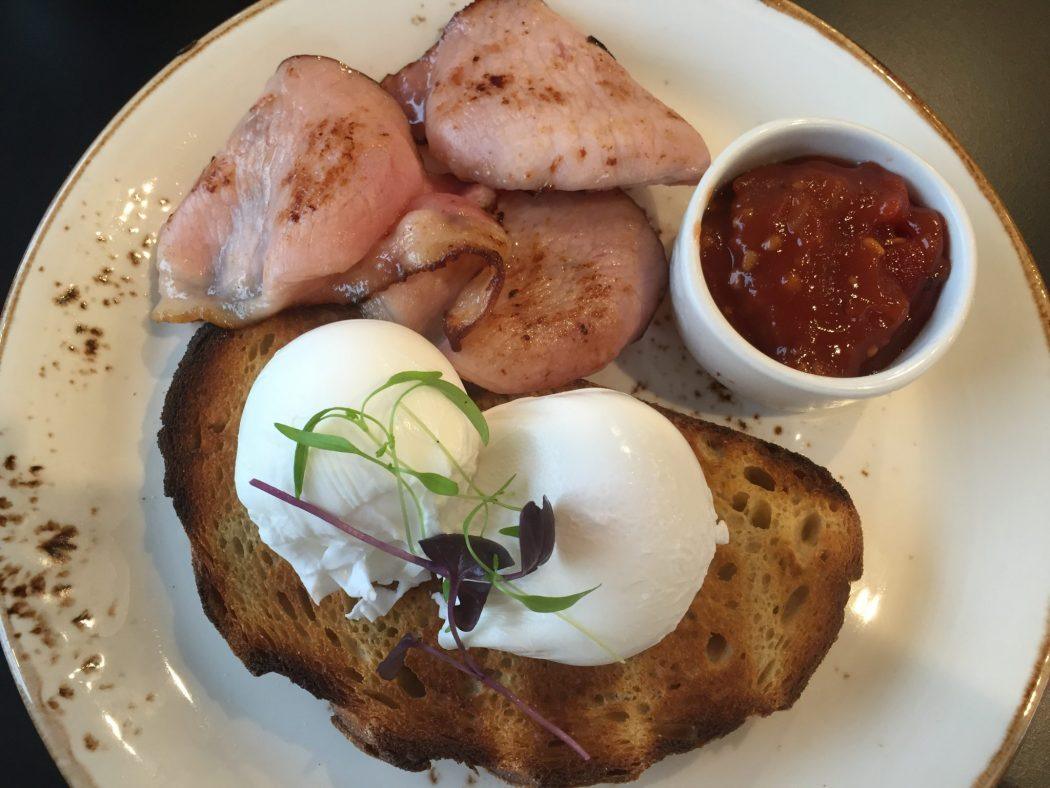 poached eggs on toast with bacon and tomato relish on a white plate
