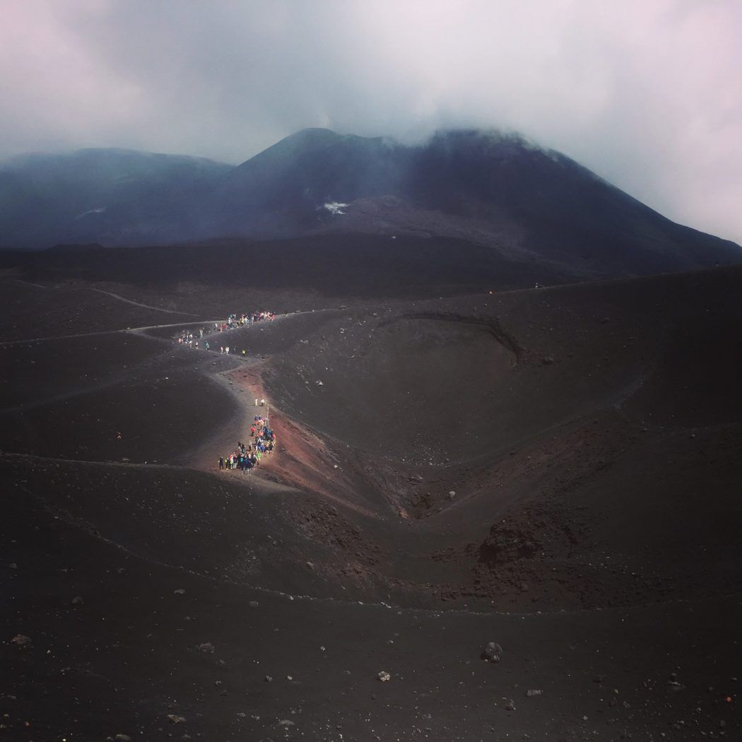 människor på avstånd klättrar upp en mörk mount Etna Sicilien