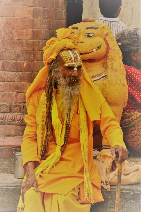 old man in full bright yellow costume sitting by the side of durbar square in Kathmandu