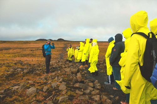 Man in cold weather gear explaining something to people in bright raincoats on a lava field in Iceland