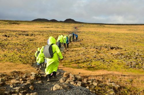 People in raincoats trekking across a lava field towards a volcano ICeland