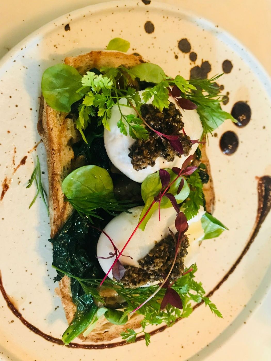 toast with poached eggs, greens and pesto on a white plate