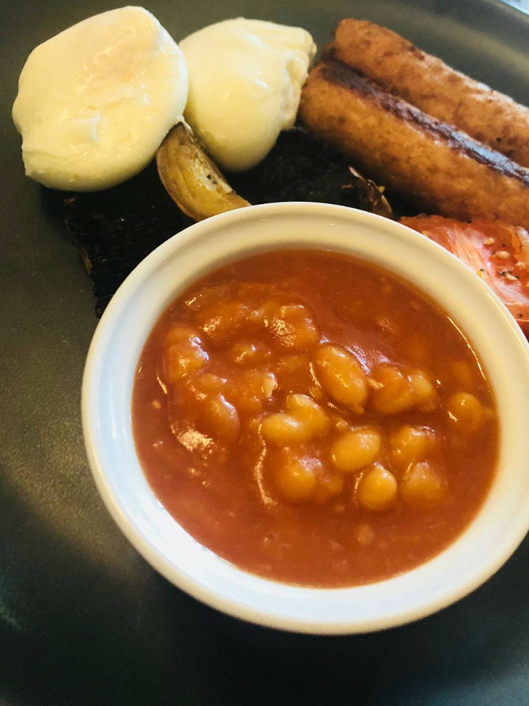 baked beans in a white bowl with poached eggs and sausages