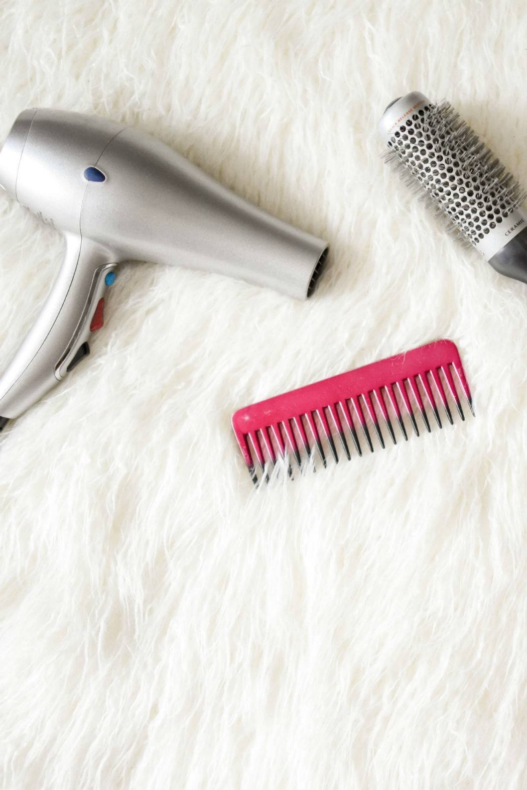 hair dryer, blow dry brush and pink comb on a white shaggy carpet