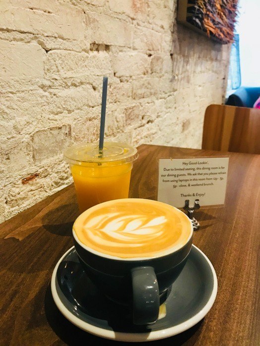 cafe latte in a grey cup and saucer with orange juice on a table