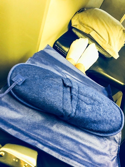 feet on the end of a business class seat with slippers on top