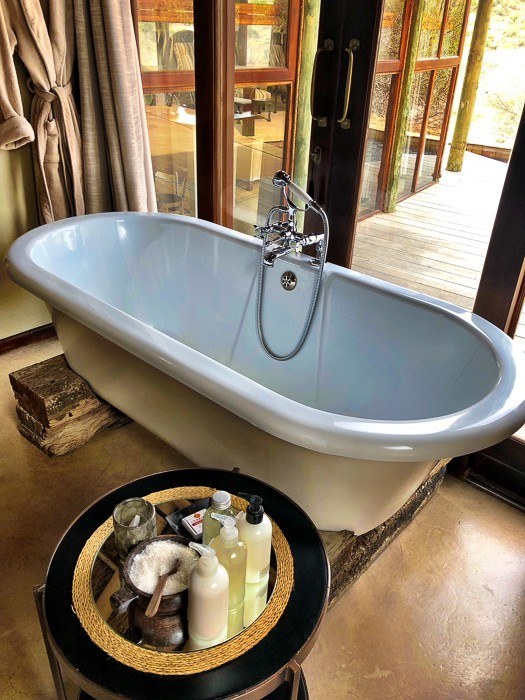 Travel Expert Packing List for Safari 22 bathtub with glass wall behind and table with toiletries in front at kwandwe