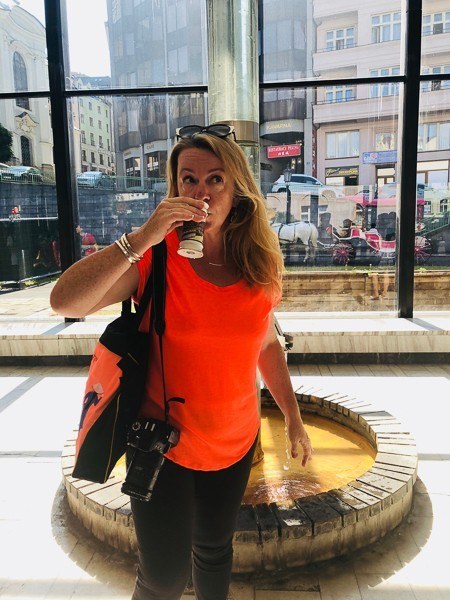 3 Best Czech Republic Spa Towns in Bohemia 6 woman in bright coral tshirt drinking from a spa cup in karlovy vary