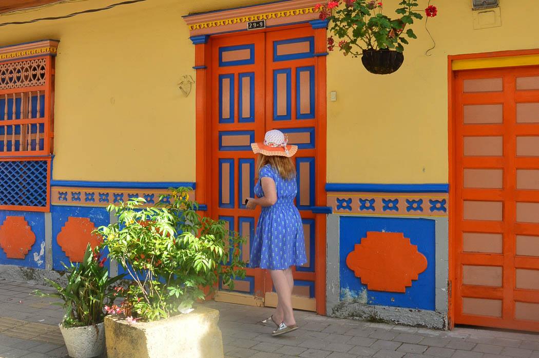 woman in hat in front of colourful door and building in guatape colombia