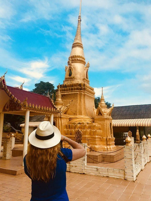 woman taking photo of golden statue in thailand