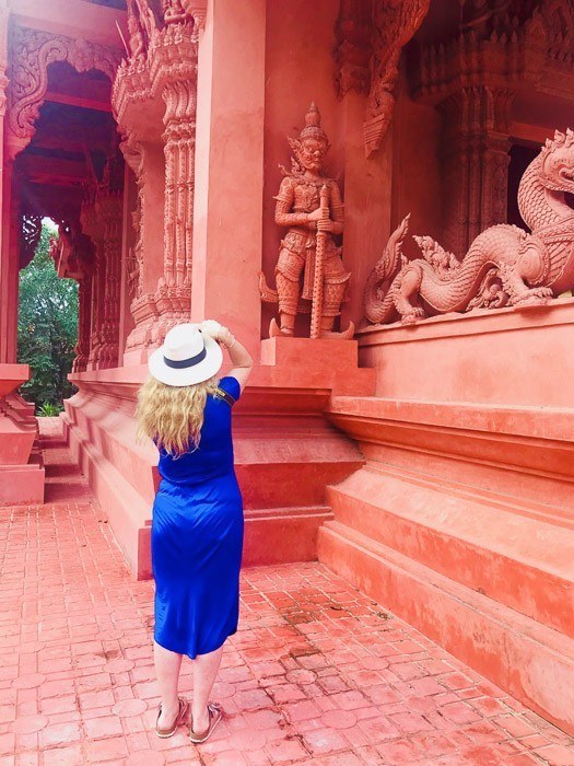 woman in panama hat take a photo of a red temple in thailand - taken from behind