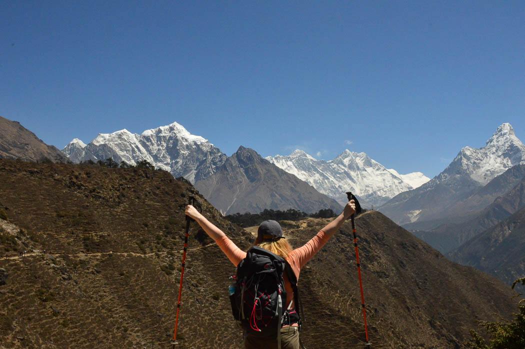 woman holding hands up with walking poles from behind with mt everest in the background in nepal