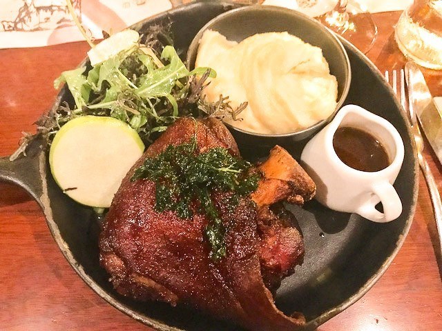 lamb shank with mashed potato and jug of gravy on a saucepan plate
