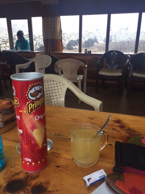 tin of pringles and a ginger lemon and honey drink on a wooden table in a tea house on the way to everest base camp