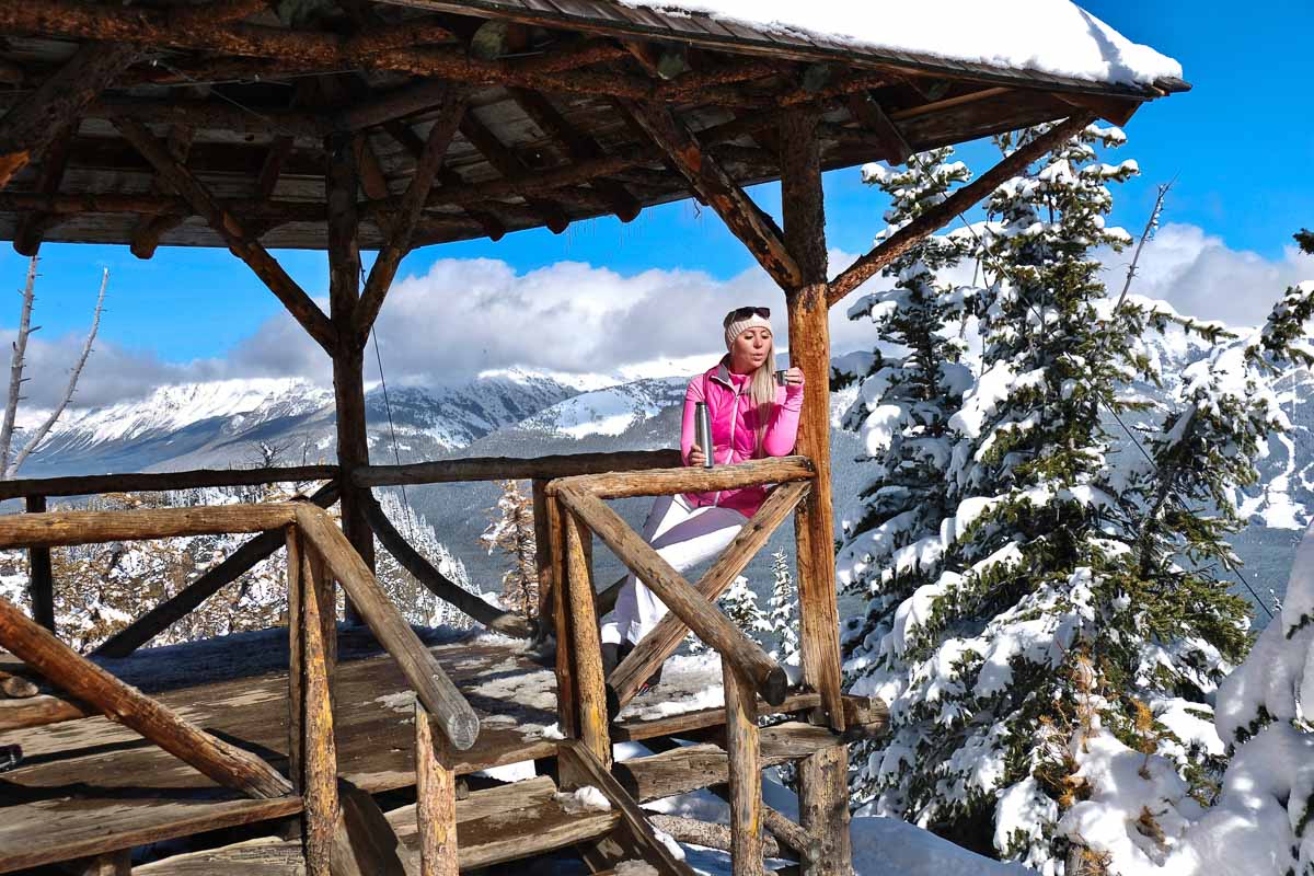 Woman skier drinking tea from thermos in open veranda on mountai