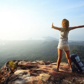 Young woman with backpack standing on cliff's edge and looking t