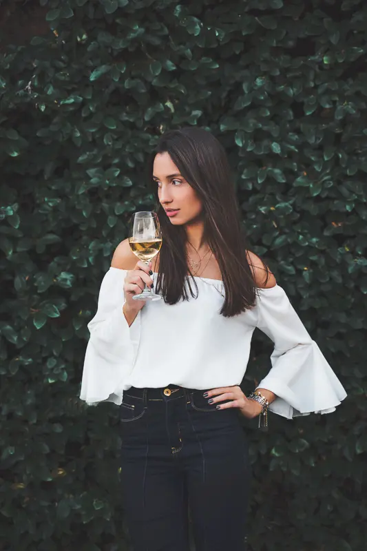 woman in off the shoulder top holding a glass of white wine