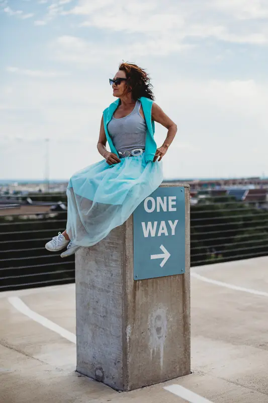 woman sits on top of pillar with one way sign on it