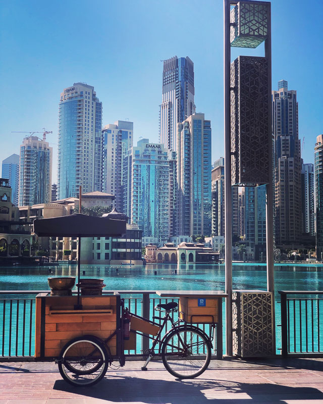 bicycle and cart in front of water and dubai syscrapers